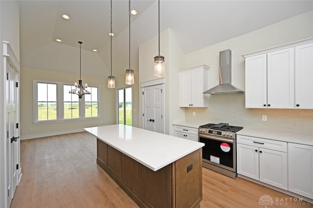 kitchen featuring wall chimney range hood, light wood-type flooring, stainless steel gas range, hanging light fixtures, and white cabinets