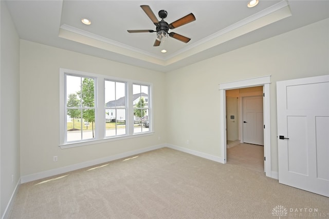 spare room with a raised ceiling, ornamental molding, and light colored carpet