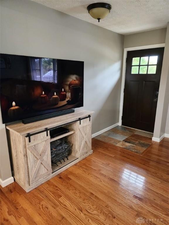 foyer entrance featuring a textured ceiling, baseboards, and wood finished floors