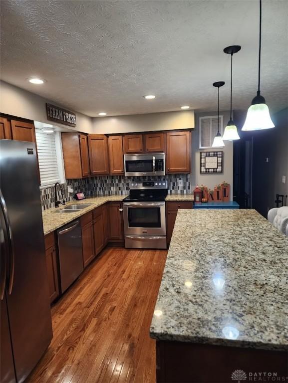 kitchen with light stone counters, wood finished floors, a sink, stainless steel appliances, and backsplash