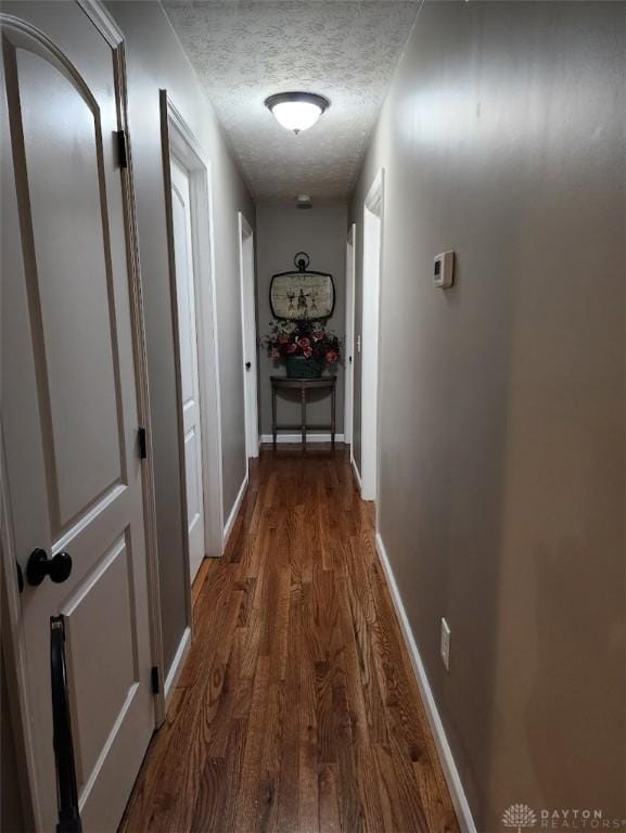 hallway featuring a textured ceiling, baseboards, and wood finished floors