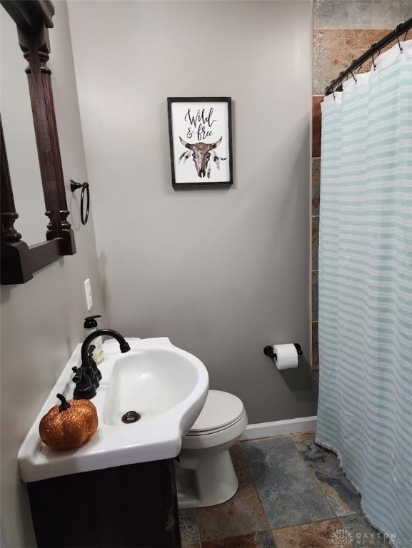 full bath with baseboards, toilet, a shower with curtain, stone tile flooring, and vanity