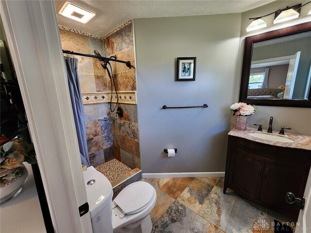 bathroom featuring vanity, stone tile floors, baseboards, tiled shower, and toilet