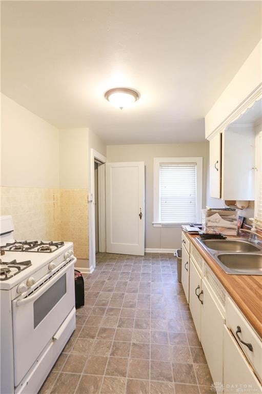 kitchen featuring sink, white gas range, and white cabinetry