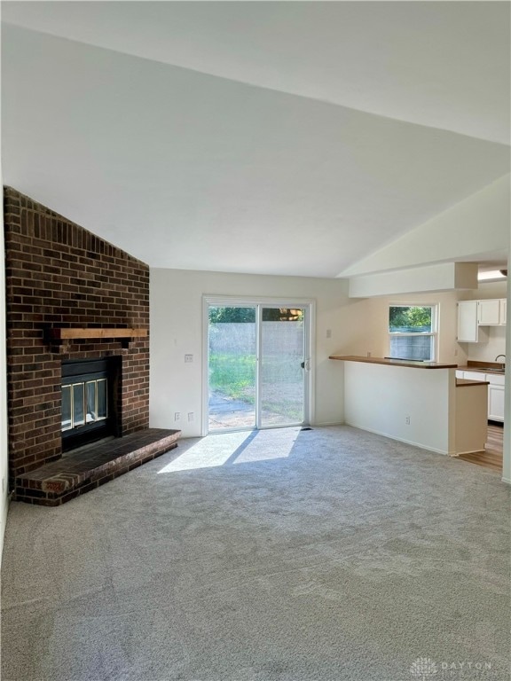 unfurnished living room with light carpet, a wealth of natural light, a fireplace, and vaulted ceiling