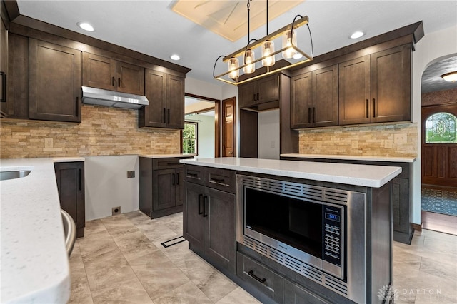 kitchen with stainless steel microwave, hanging light fixtures, backsplash, and dark brown cabinets