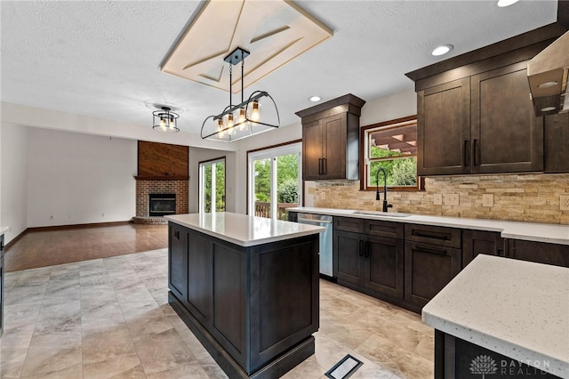 kitchen with sink, stainless steel dishwasher, a textured ceiling, decorative light fixtures, and a center island