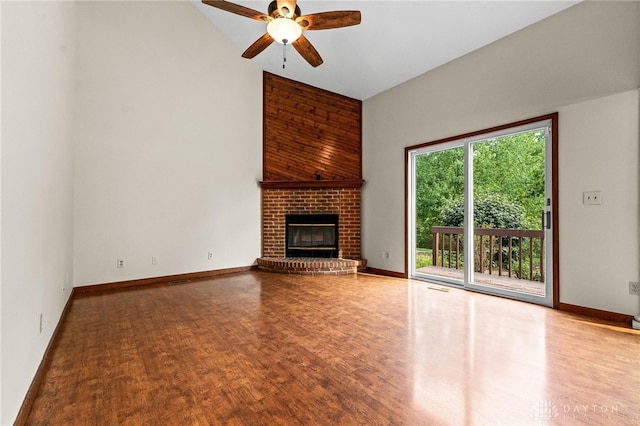 unfurnished living room with a towering ceiling, a brick fireplace, hardwood / wood-style floors, and ceiling fan