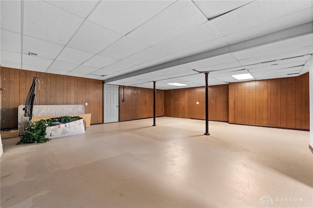 basement featuring wood walls and a drop ceiling