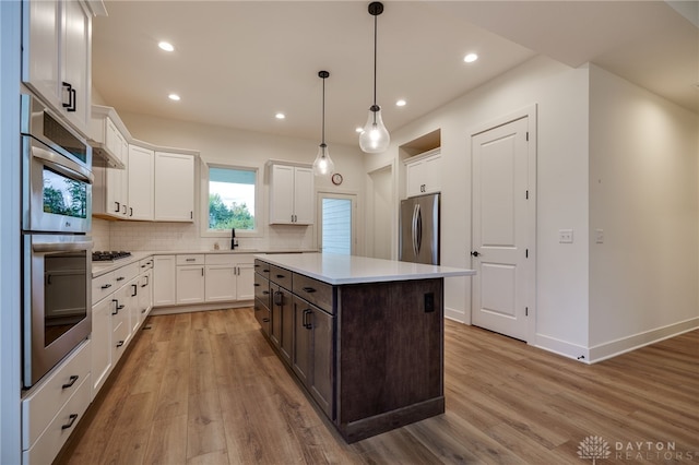 kitchen with appliances with stainless steel finishes, light wood-type flooring, white cabinetry, and a kitchen island