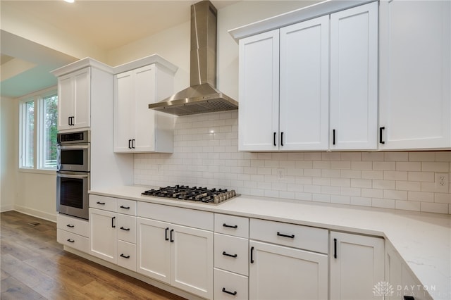 kitchen featuring wall chimney exhaust hood, appliances with stainless steel finishes, light hardwood / wood-style flooring, and white cabinetry