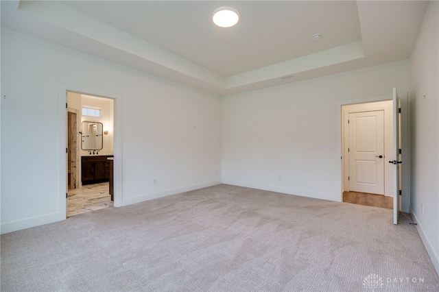 unfurnished bedroom with light carpet, ensuite bath, and a tray ceiling