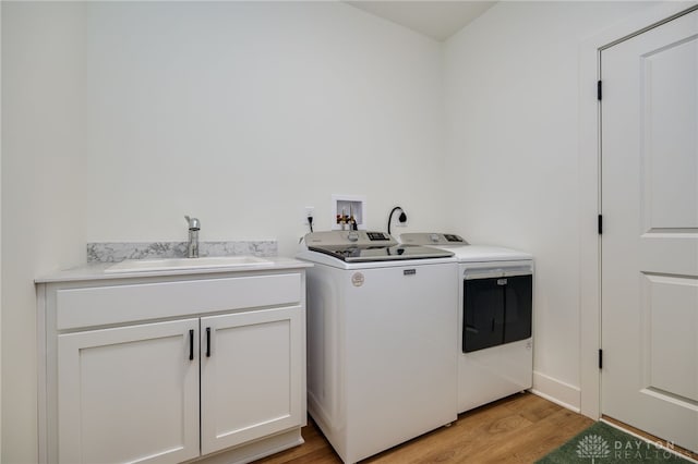 laundry room featuring cabinets, washer and clothes dryer, sink, and light hardwood / wood-style flooring