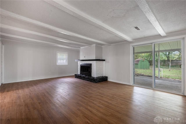 unfurnished living room featuring a brick fireplace, a textured ceiling, wood-type flooring, and beamed ceiling