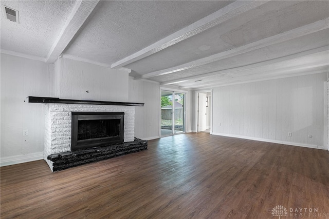 unfurnished living room with a brick fireplace, wood walls, beam ceiling, dark wood-type flooring, and a textured ceiling