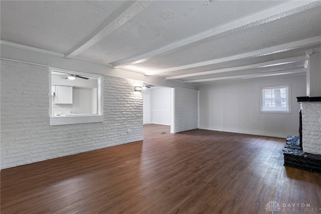 unfurnished living room featuring ceiling fan, a brick fireplace, dark hardwood / wood-style floors, a textured ceiling, and beam ceiling