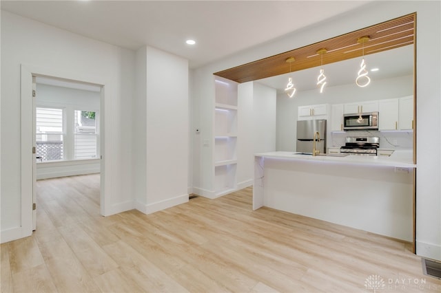 kitchen with appliances with stainless steel finishes, decorative light fixtures, white cabinetry, tasteful backsplash, and light hardwood / wood-style flooring