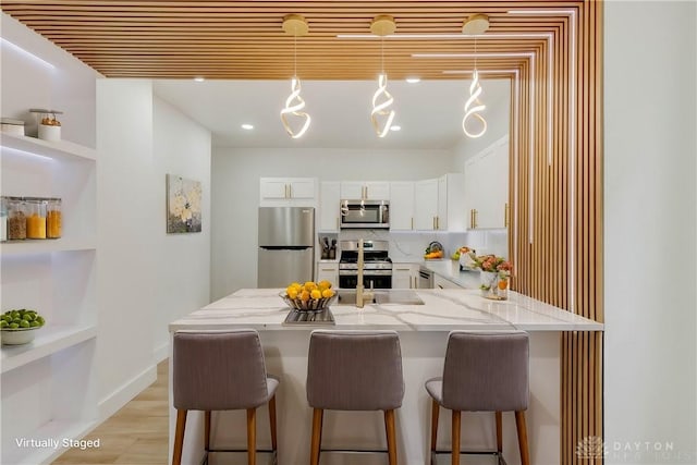 kitchen with light stone counters, pendant lighting, white cabinets, and stainless steel appliances