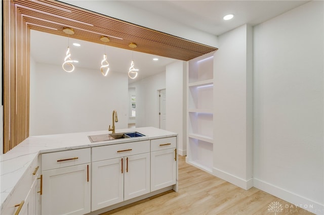 bar with decorative light fixtures, light stone countertops, sink, and white cabinetry