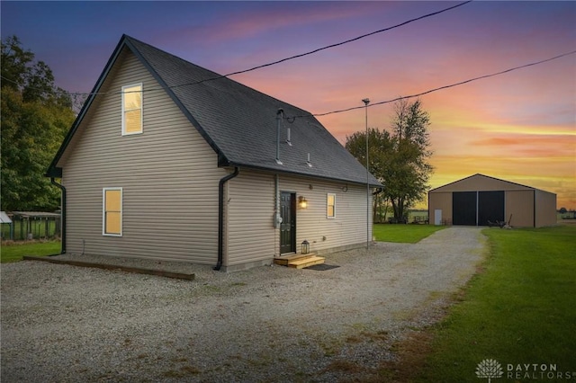 back house at dusk featuring a lawn and an outbuilding