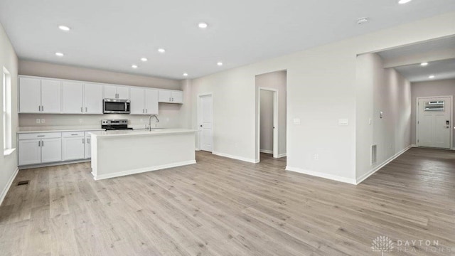 kitchen featuring white cabinetry, sink, stainless steel appliances, light hardwood / wood-style floors, and a center island with sink