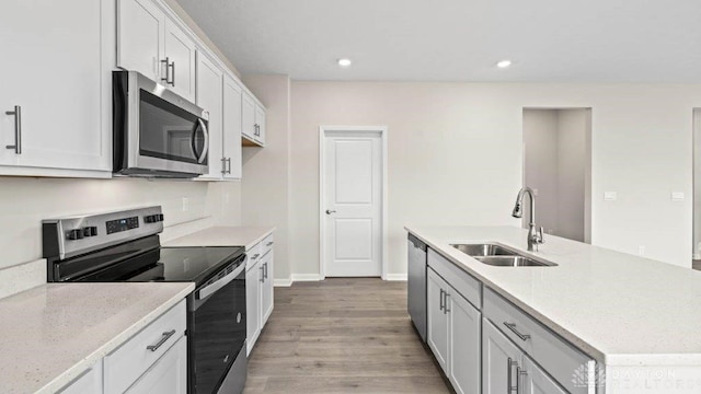 kitchen with light stone counters, stainless steel appliances, sink, white cabinets, and light hardwood / wood-style floors