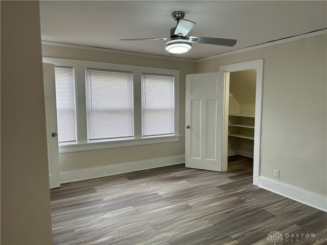 unfurnished bedroom with hardwood / wood-style flooring, a closet, a walk in closet, crown molding, and ceiling fan