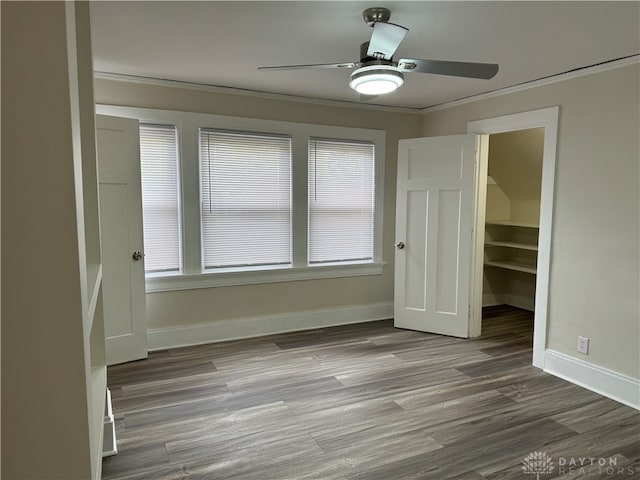 unfurnished bedroom featuring a closet, wood-type flooring, a spacious closet, ornamental molding, and ceiling fan