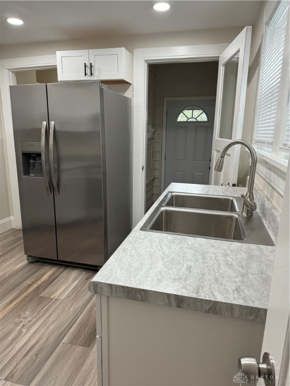 kitchen featuring white cabinets, light hardwood / wood-style flooring, sink, and stainless steel fridge