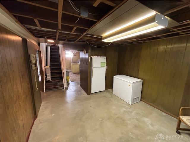 basement with wood walls, refrigerator, and white fridge