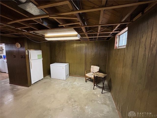 basement with washer / clothes dryer, wood walls, and white fridge