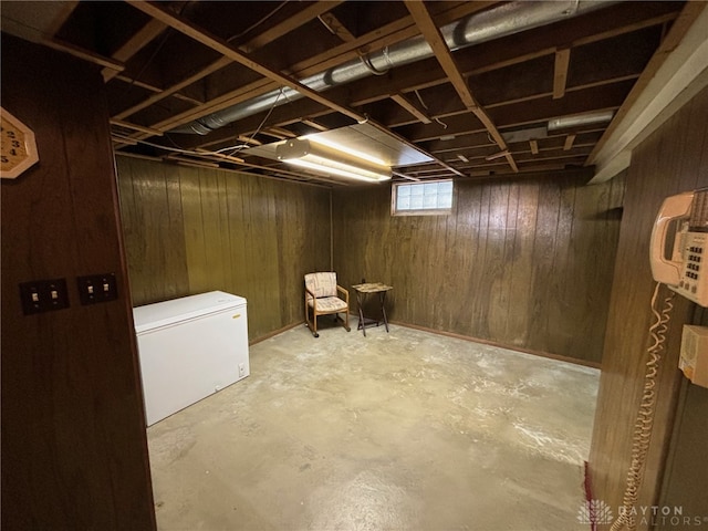 basement featuring refrigerator and wooden walls