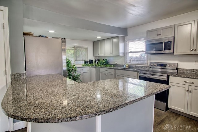 kitchen with dark wood-type flooring, stone counters, a kitchen breakfast bar, sink, and appliances with stainless steel finishes