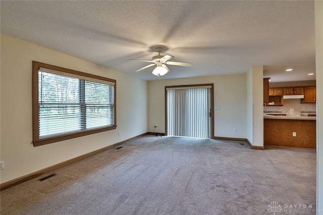 interior space with light carpet, a textured ceiling, ensuite bath, and ceiling fan