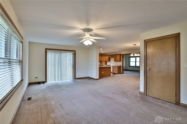 unfurnished living room featuring ceiling fan with notable chandelier, a textured ceiling, and light carpet