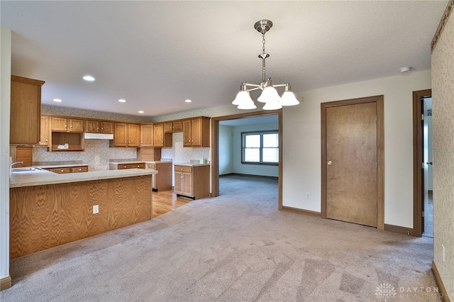 kitchen featuring sink, an inviting chandelier, kitchen peninsula, decorative light fixtures, and light carpet