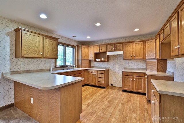 kitchen with kitchen peninsula, a textured ceiling, light hardwood / wood-style floors, and sink