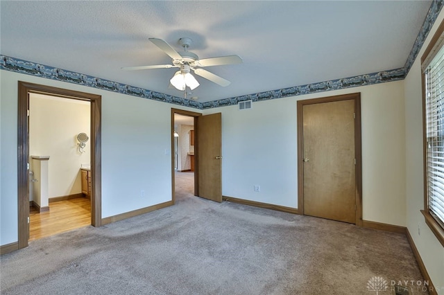 unfurnished bedroom featuring light carpet, a textured ceiling, connected bathroom, and ceiling fan