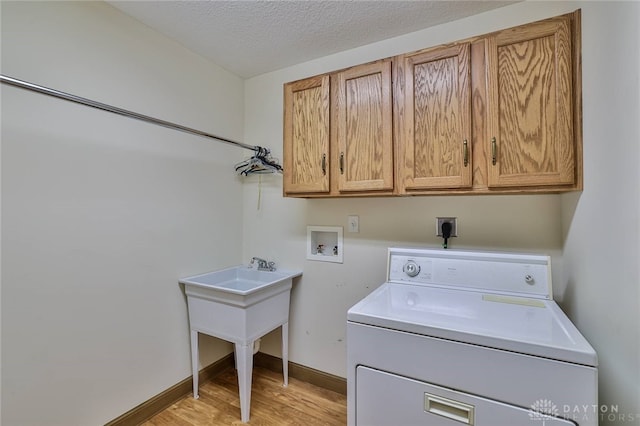 laundry room featuring cabinets, a textured ceiling, washer / clothes dryer, and light hardwood / wood-style flooring