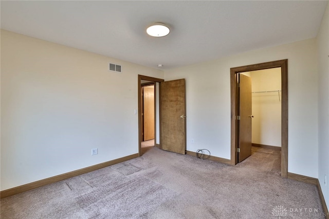 unfurnished bedroom with a spacious closet, a closet, and light carpet