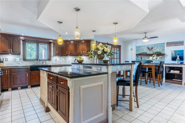 kitchen featuring a kitchen island, a kitchen bar, decorative light fixtures, light tile patterned flooring, and dark stone counters