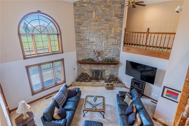 living room with a high ceiling, a stone fireplace, carpet, and ceiling fan