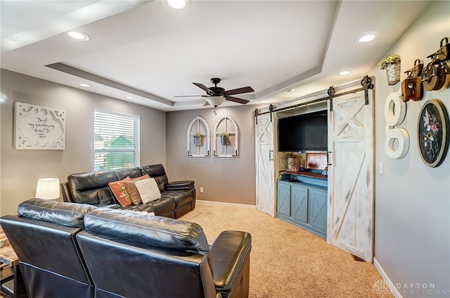 living room featuring a barn door, ceiling fan, a tray ceiling, and light colored carpet