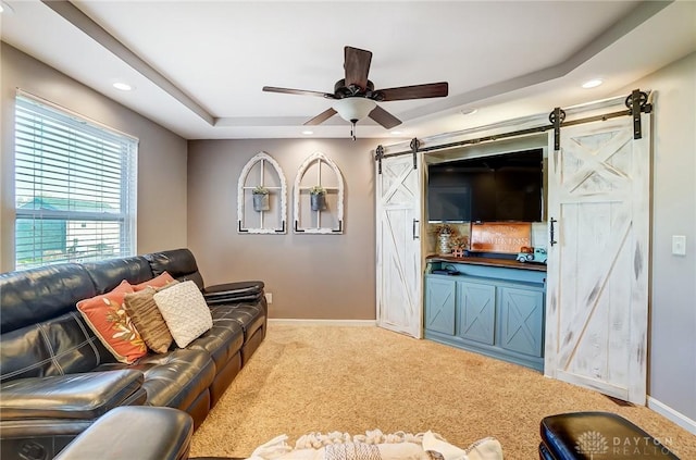 living room with carpet, a ceiling fan, baseboards, a tray ceiling, and a barn door