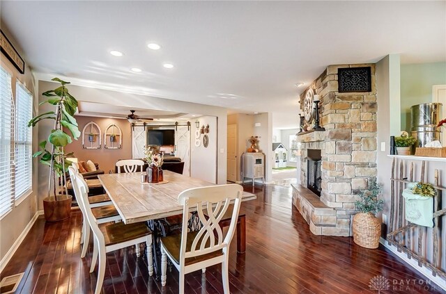 dining room with a barn door, dark wood-type flooring, a fireplace, and ceiling fan