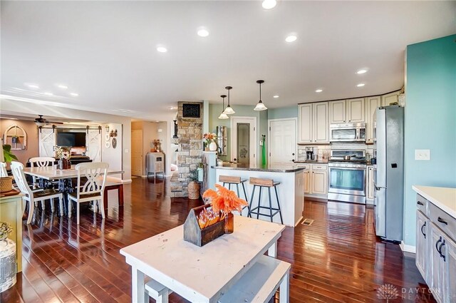 kitchen with tasteful backsplash, hanging light fixtures, ceiling fan, stainless steel appliances, and dark wood-type flooring