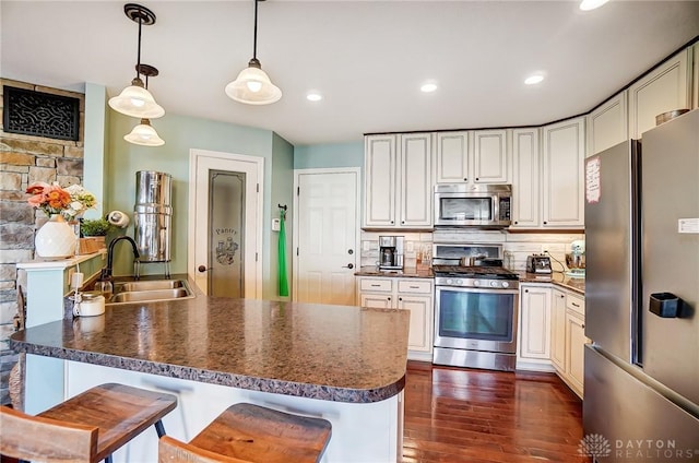 kitchen featuring dark countertops, dark wood-type flooring, decorative backsplash, appliances with stainless steel finishes, and a sink