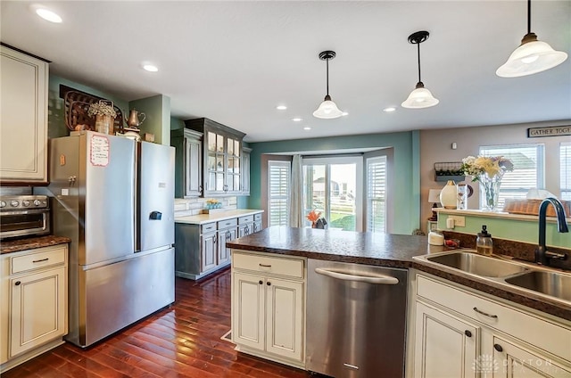 kitchen with a sink, dark wood-type flooring, appliances with stainless steel finishes, pendant lighting, and dark countertops