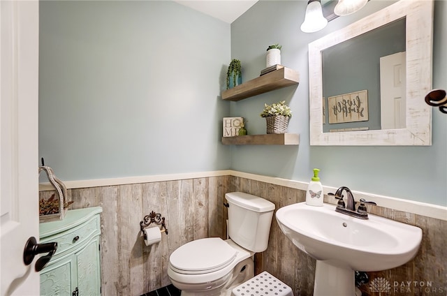 bathroom featuring toilet, wood walls, and sink