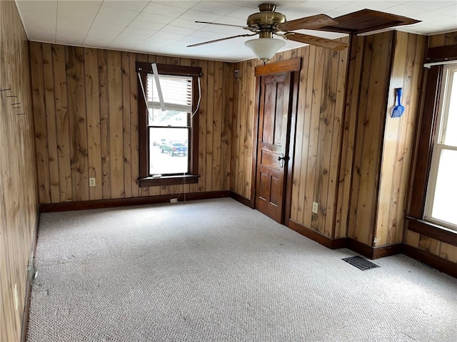 carpeted spare room featuring ceiling fan and wood walls